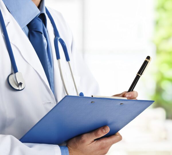 A male doctor writes on a clipboard and has a stethoscope around his neck.